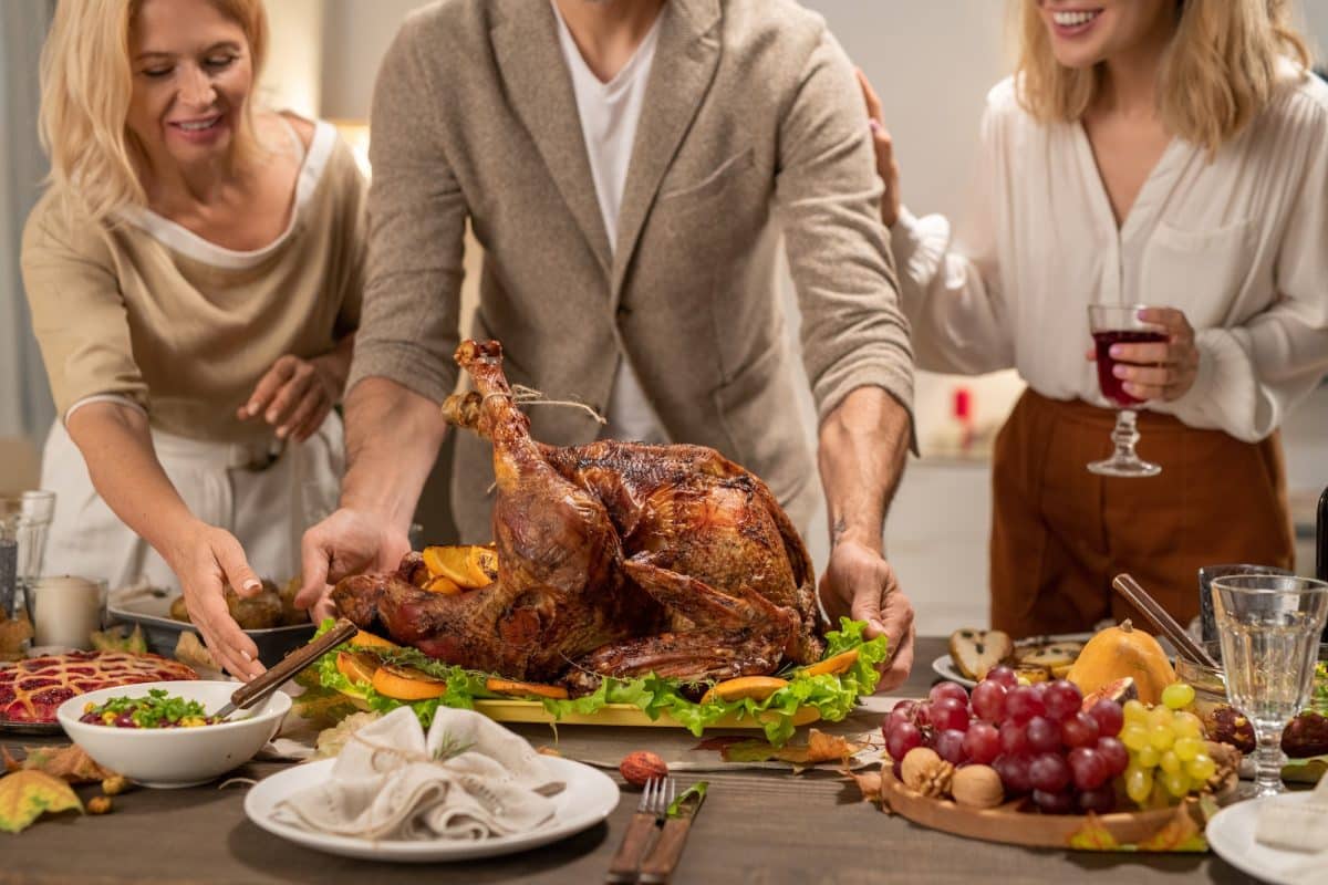Young and mature females surrounding man putting big roasted turkey on table