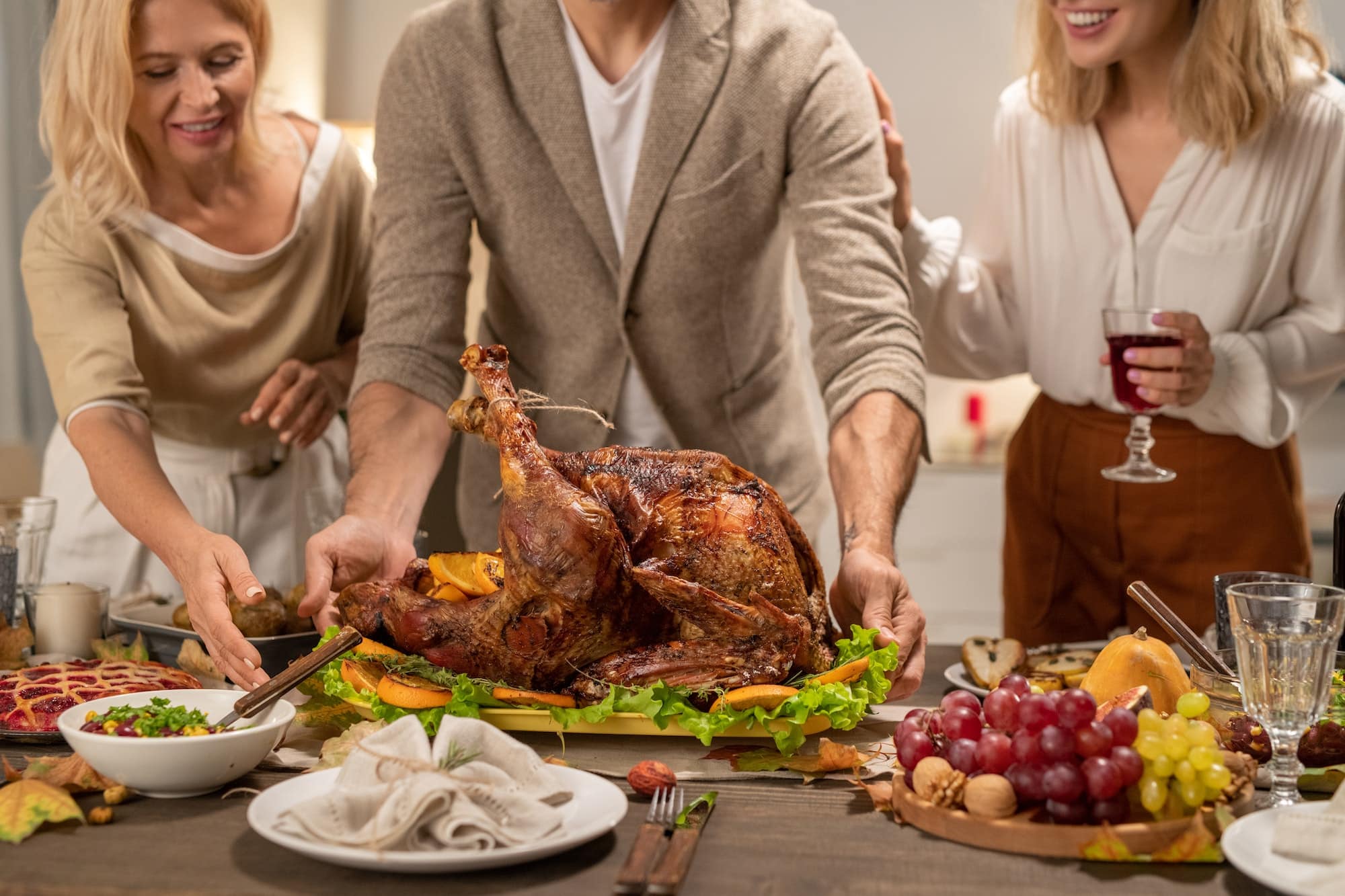 Young and mature females surrounding man putting big roasted turkey on table