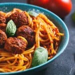 Close-up of Italian pasta with tomato sauce and meatballs in blue plate.
