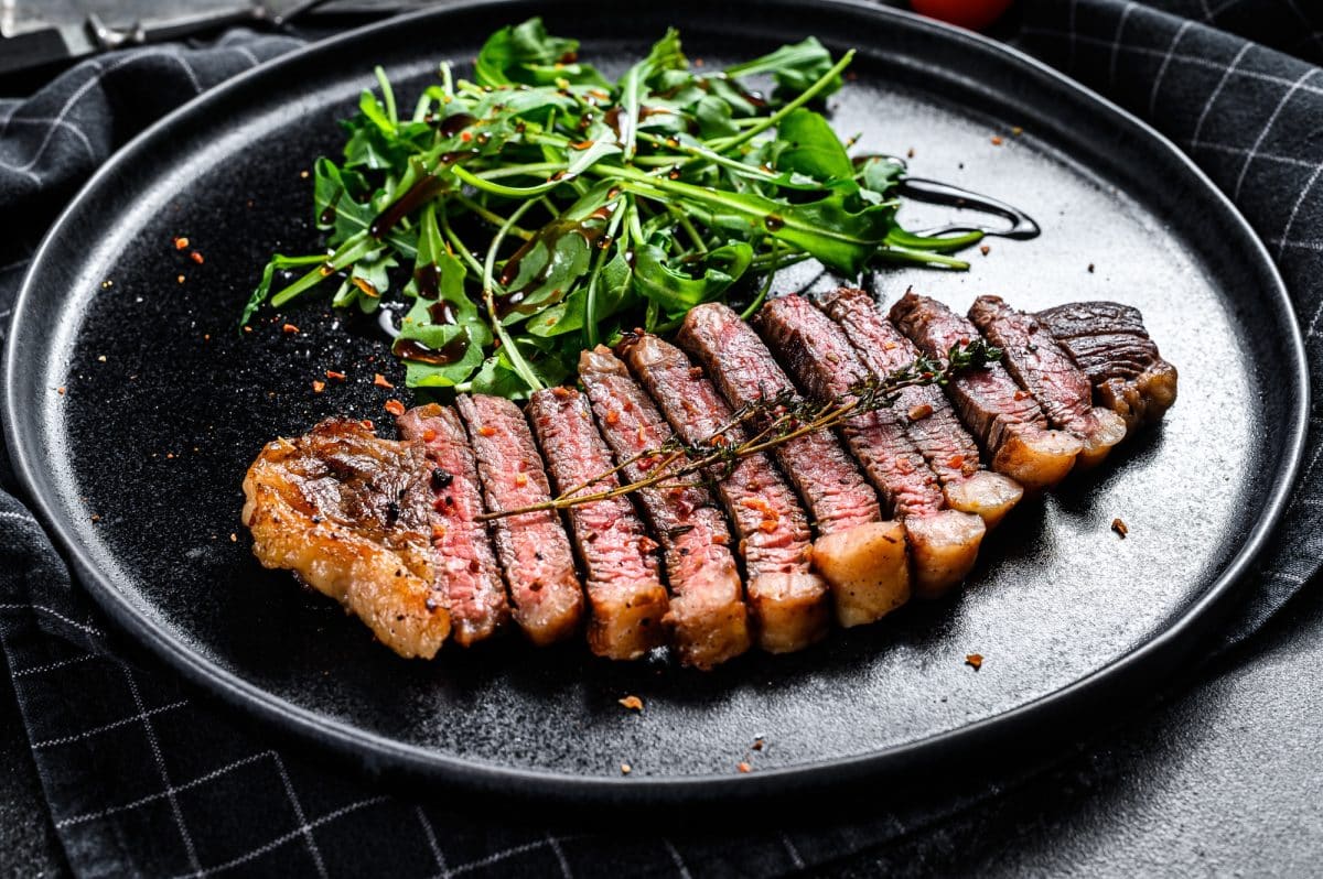 Fillet entrecote steak, marbled beef meat with arugula. Black background. Top view