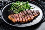 Fillet entrecote steak, marbled beef meat with arugula. Black background. Top view