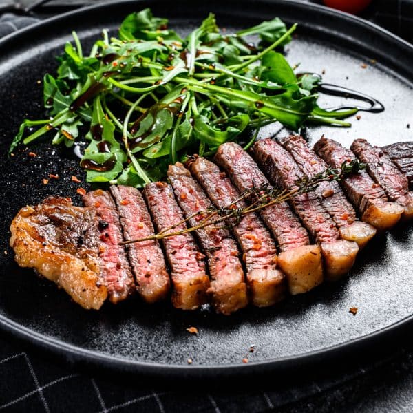 Fillet entrecote steak, marbled beef meat with arugula. Black background. Top view