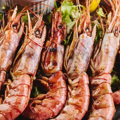 Grilled king prawns with sauce on platter close up.